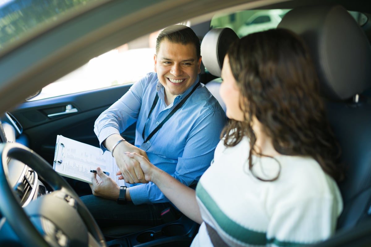 Blije rij-instructeur feliciteert zijn leerling na het behalen van het rijbewijs